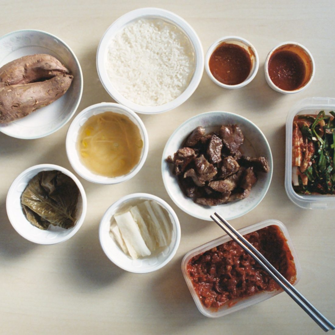 A full spread of Korean banchan side dishes in small bowls, ready to refill at the table